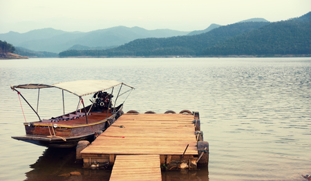 Thai motor boat at pier on mountain lake. Idyllic landscape, wanderlust background. text space.の写真素材