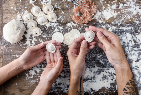 Top view mom's and daughter's hands holding fresh raw homemade dumplings. above table with ingredients. Family tradition, education concept. Cooking backgroundの写真素材