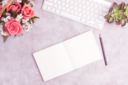 Pink roses on grey table with white keyboard and open notebook. Artist workplace, office concepr....