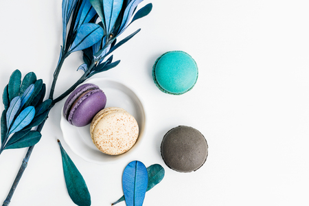 Top view flat lay colorful macarons and blue leaves on white table. Creative dessert conceptの写真素材