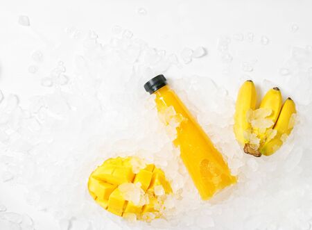 Flat lay top view colorful yellow juice bottle with bananas and mango in ice. Healthy lifestyle concept. Vegan, vegetarian foodの写真素材