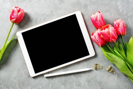 Flat lay top view mockup: digital tablet with pencil and red tulips on grey background. Text space の写真素材
