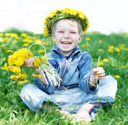 Happy kid with diadem and dandelions on green grassの写真素材