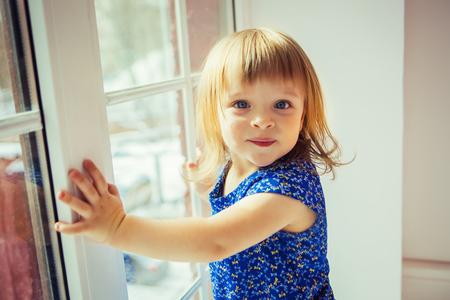 Funny little girl hold on big windowの写真素材