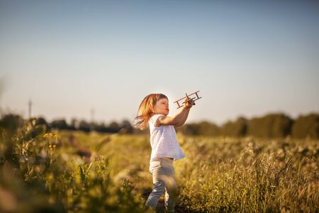 Little girl with toy wooden airplane in summer fieldの写真素材