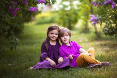 Beautiful kids twins boy and girl in spring garden with lilacの写真素材
