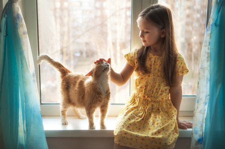 Happy twins with redhead cat at window in cozy homeの写真素材