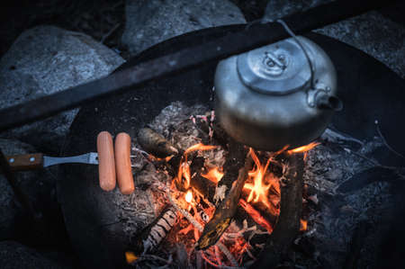 Metal kettle and grilled sausage on a campfireの写真素材