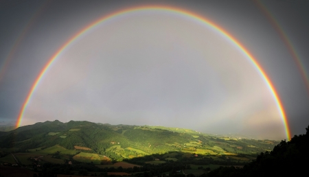 Full double rainbow with sunlit hills and fields through the arc of the rainbowの写真素材