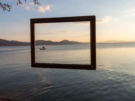 A fisherman captured in a frame after  tending his nets on Lago Trasimeno, Perugia, Italy at dusk   The lake is a shallow muddy lake abundant with fishの写真素材