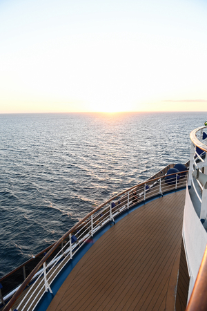 Railing and deck flooring of a cruise ship at sunset with the ocean in the background.の写真素材