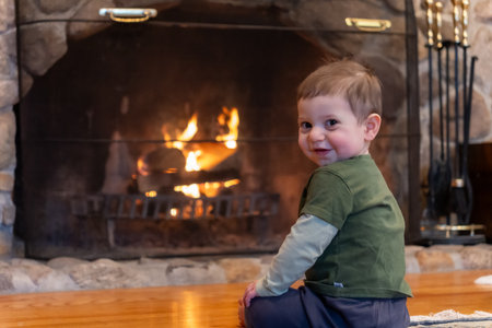 Cute little boy sitting on the floor in front of the fireplaceの写真素材