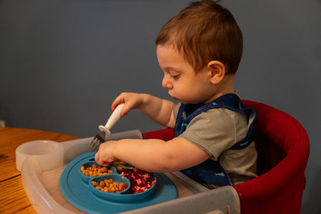 Cute baby boy eating food in high chair at homeの写真素材