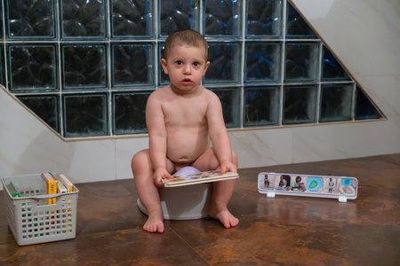 Cute baby boy in diaper sitting on toilet and looking at camera