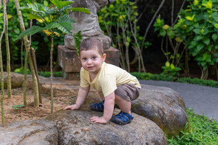 Cute baby boy sitting on a rock in a tropical garden.の写真素材