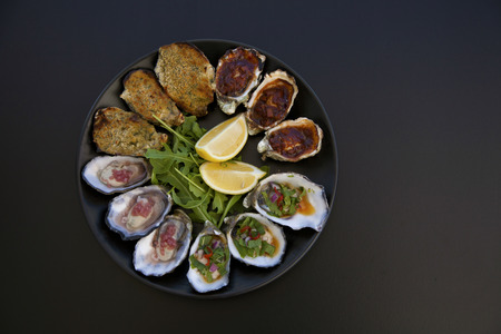 A plate of oysters 4 ways on a black background taken from above.の写真素材