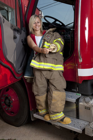 A female firefighter standing in the door of a fire truck.
