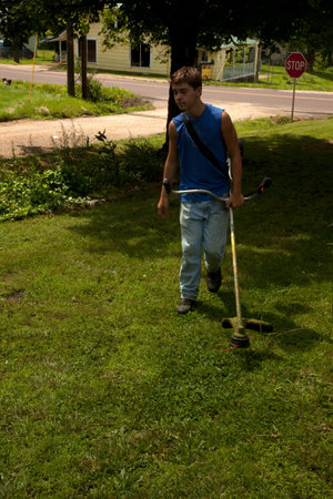 A teenage boy weed eating a yard.