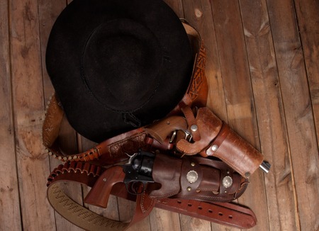A cowboy hat and pistol on a wooden background.の写真素材