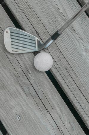Well-used golf club pitching wedge (marked "P") and golf ball on a weathered wooden deck.の写真素材