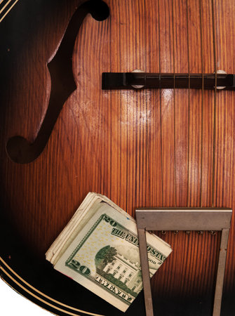Detail view of old, beat-up acoustic guitar, with a wad of U.S. paper money stuck in the tailpoece.