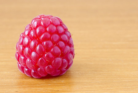Single red ripe raspberry on wooden table