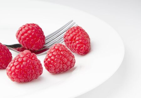 Red ripe raspberries on a plate with a forkの写真素材