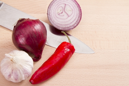 Red onion, chilli, garlic and knife on wooden chopping boardの写真素材