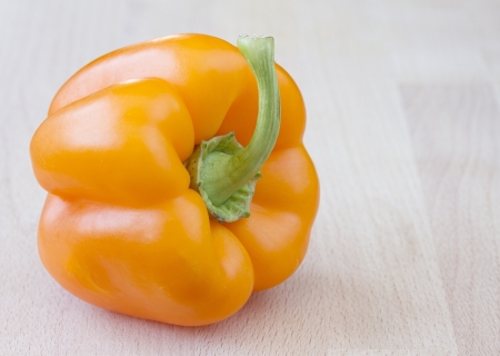 Orange pepper on wooden chopping blockの写真素材