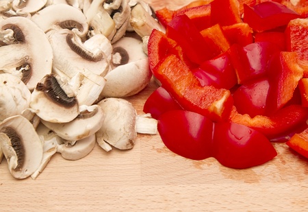Fresh chopped mushrooms and red peppers on wooden chopping boardの写真素材