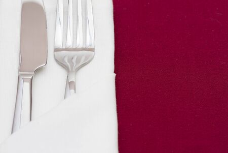 Shiny cutlery in folded white napkin on red tableclothの写真素材