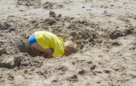 Young blond boy digging a hole in the beachの写真素材