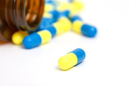 Yellow and blue pills with brown bottle on whiteの写真素材