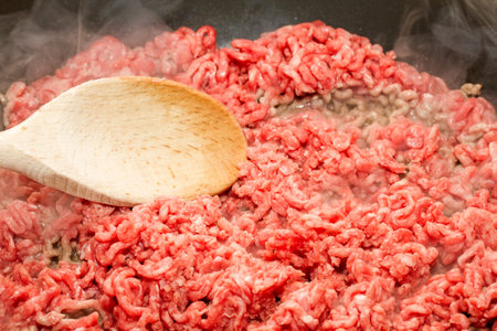 Raw mince starting to brown in pan with wooden spoon