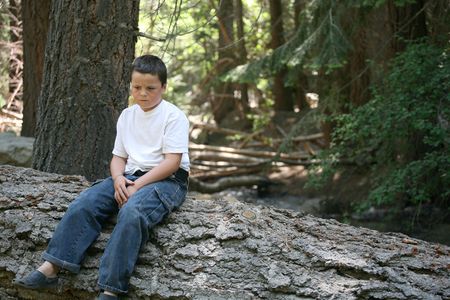 Young boy that appears sad to be sitting on this log in the forestの写真素材