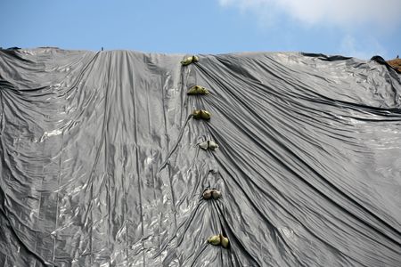 Plastic covered hill and sand bags with beautiful blue cloudy skyの写真素材