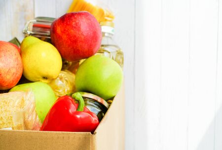 Donation box with various food. Open cardboard box with butter, canned goods, cereals and fruits.の写真素材