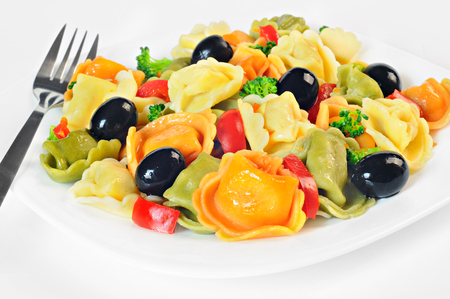 Salad made with tortellini, olives, broccoli, red pepper, on a plate, white backgroundの写真素材
