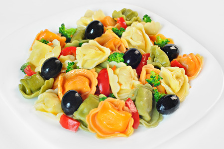 Salad made with tortellini, olives, broccoli, red pepper, on a plate, white backgroundの写真素材