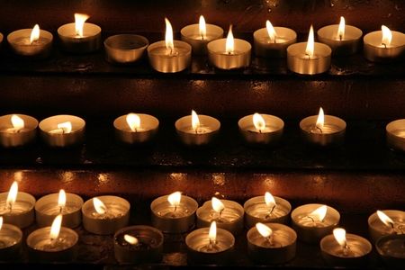Prayer candles aka offering, votive or memorial candles lit in a dark churchの写真素材