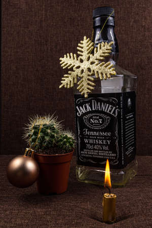 Riga, Latvia- October 20 2020: Christmas greeting card concept, Jack Daniels bottle with gold shiny snowflake on it, candle fire and small cactus with gold ball, holiday background posterのeditorial素材