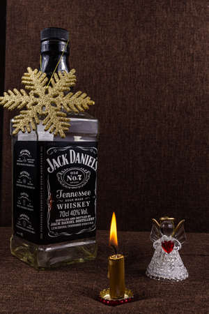 Riga, Latvia- October 20 2020: Christmas greeting card concept, Jack Daniels bottle with gold shiny snowflake on it, candle fire and white angel with red heart in hands, holiday background, greeting card.のeditorial素材