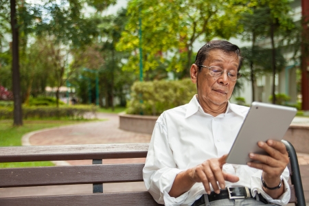An old man enjoying morning sun reading newspaper from an iPadの写真素材