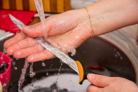 Woman washing the long knife by hands in the sink in the kitchen under clean running water