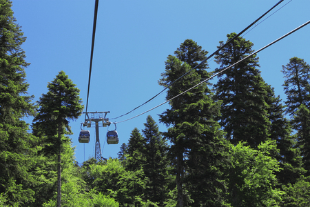 Ð¡ableway moving up between high trees and Caucasus mountains against blue skyの写真素材