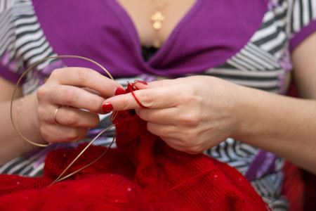 Adult woman knits with knitting needles a red sweater from natural woolen threads indoorの写真素材