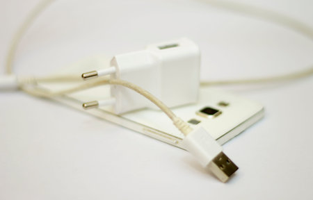 Modern white smartphone and phone charge with power cord isolated on the white bckground