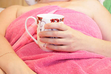 Woman in pink towel after bathing drinking coffee from white and red cupの写真素材