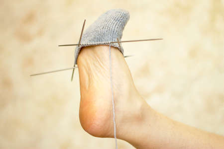 Woman tries an unfinished gray wool sock on her leg on the light backgroundの写真素材