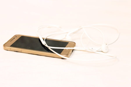 Smartphone with blank screen and white earphones on the white background side view. Device and...